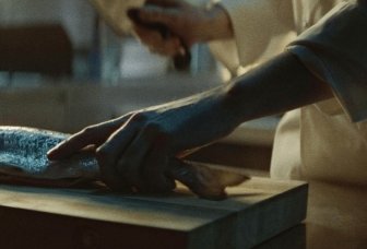 Person skär en fisk på en träskiva. Foto