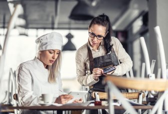Kvinnlig kock och servitris tittar på ipad och använder kalkylator. Foto